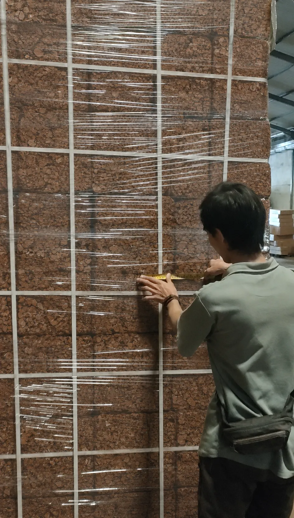 Checking a wrapped pallet of coco husk chips blocks with a measuring tape before shipment